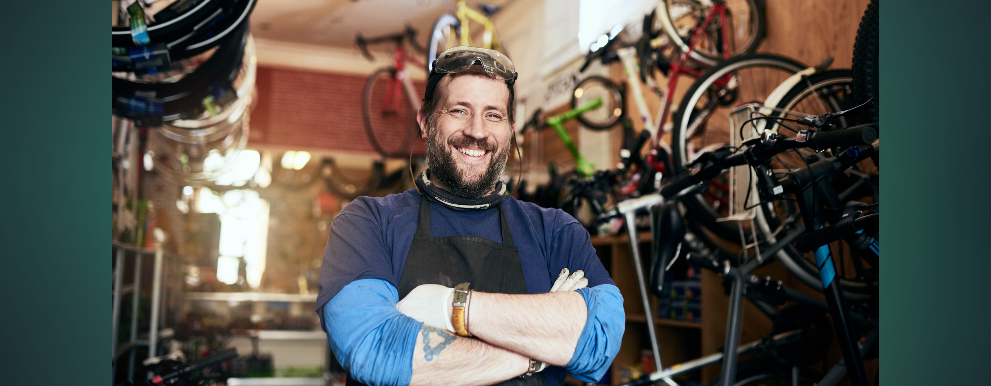 A smiling bike shop owner standing in his workshop, surrounded by bicycles.