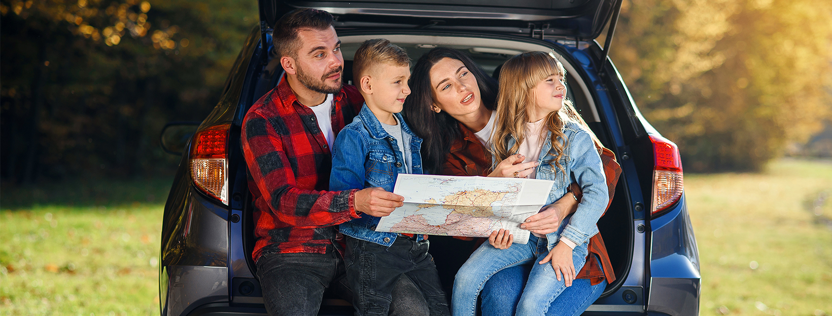 A family sitting on the ledge of their car looking at a map together