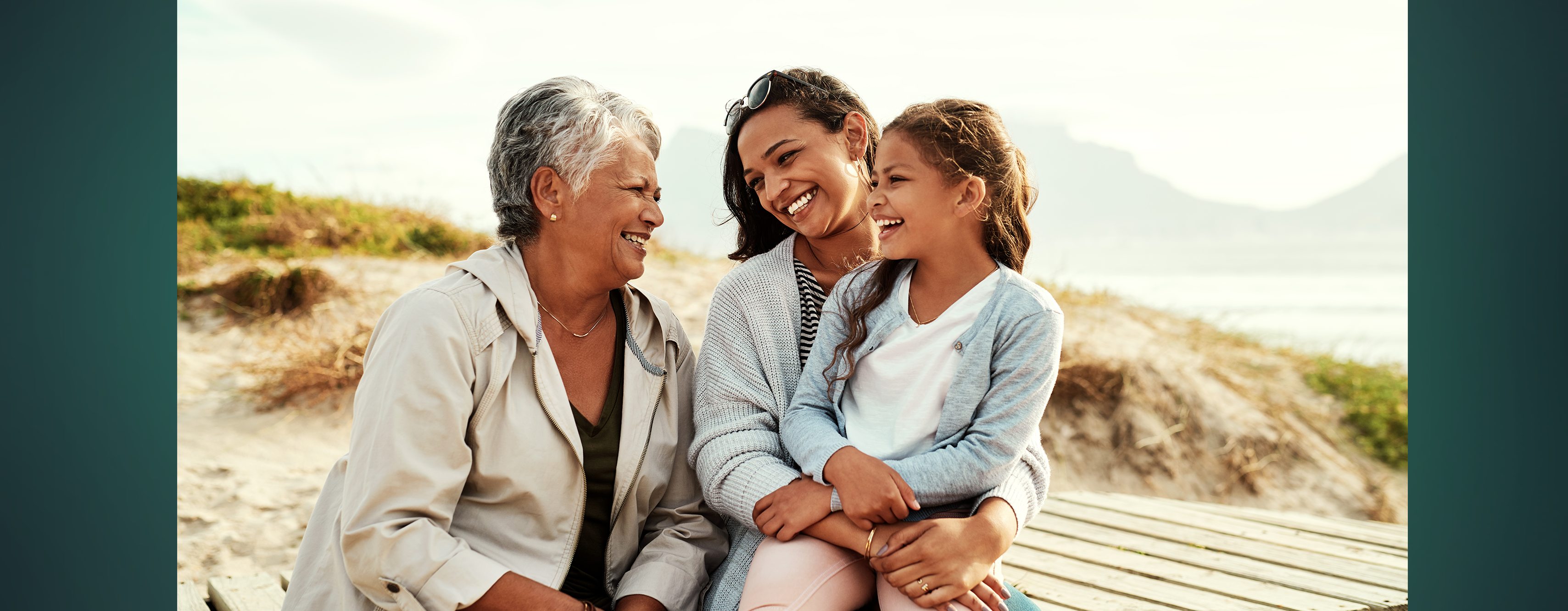A mother, young daughter and grandmother sitting outside together smiling