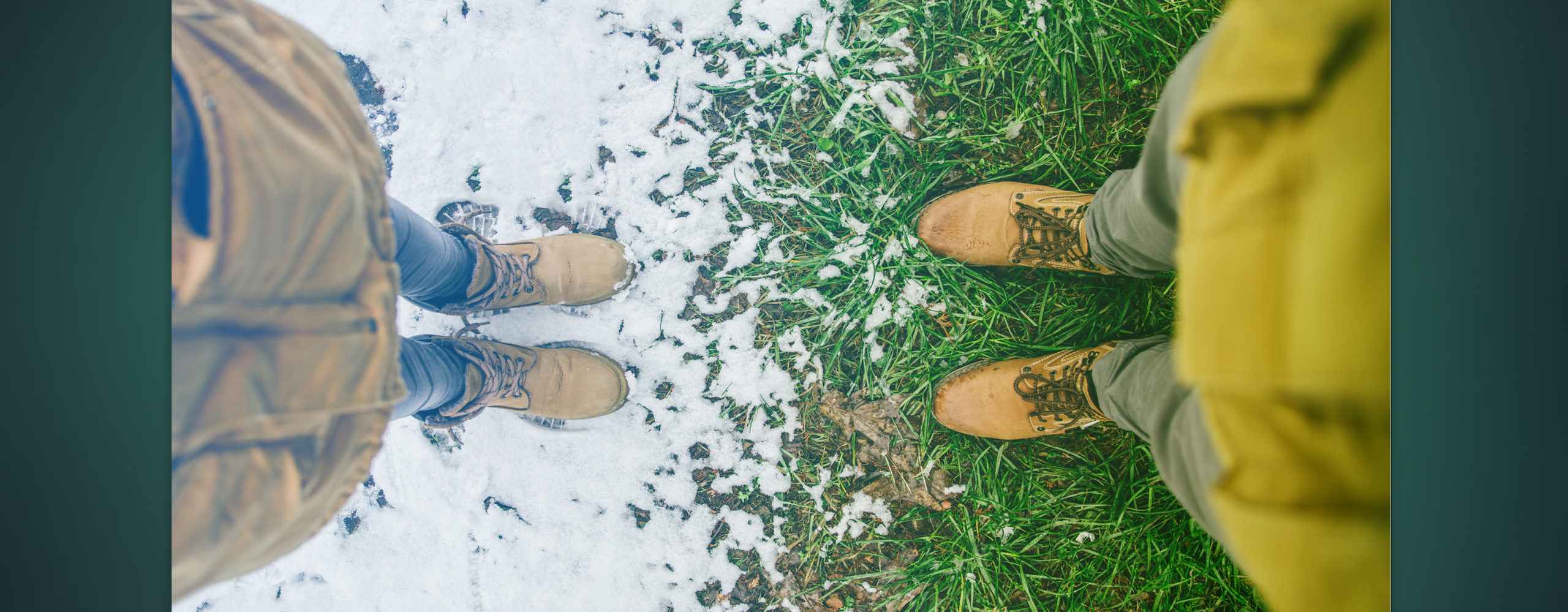 A top-down photo of two people wearing winter boots, facing each other. They stand on a sharp contrast line where a patch of white snow meets a patch of vibrant green grass.