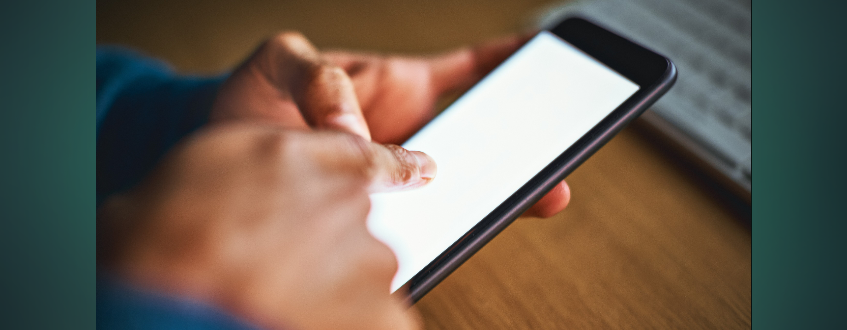 A close up photo of a person's hands holding a cell phone that's displaying a blank bright white screen