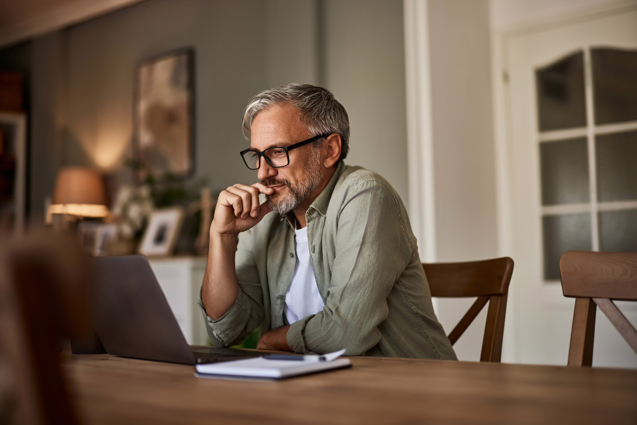 A man with gray hair sitting at a dining table looking at his laptop
