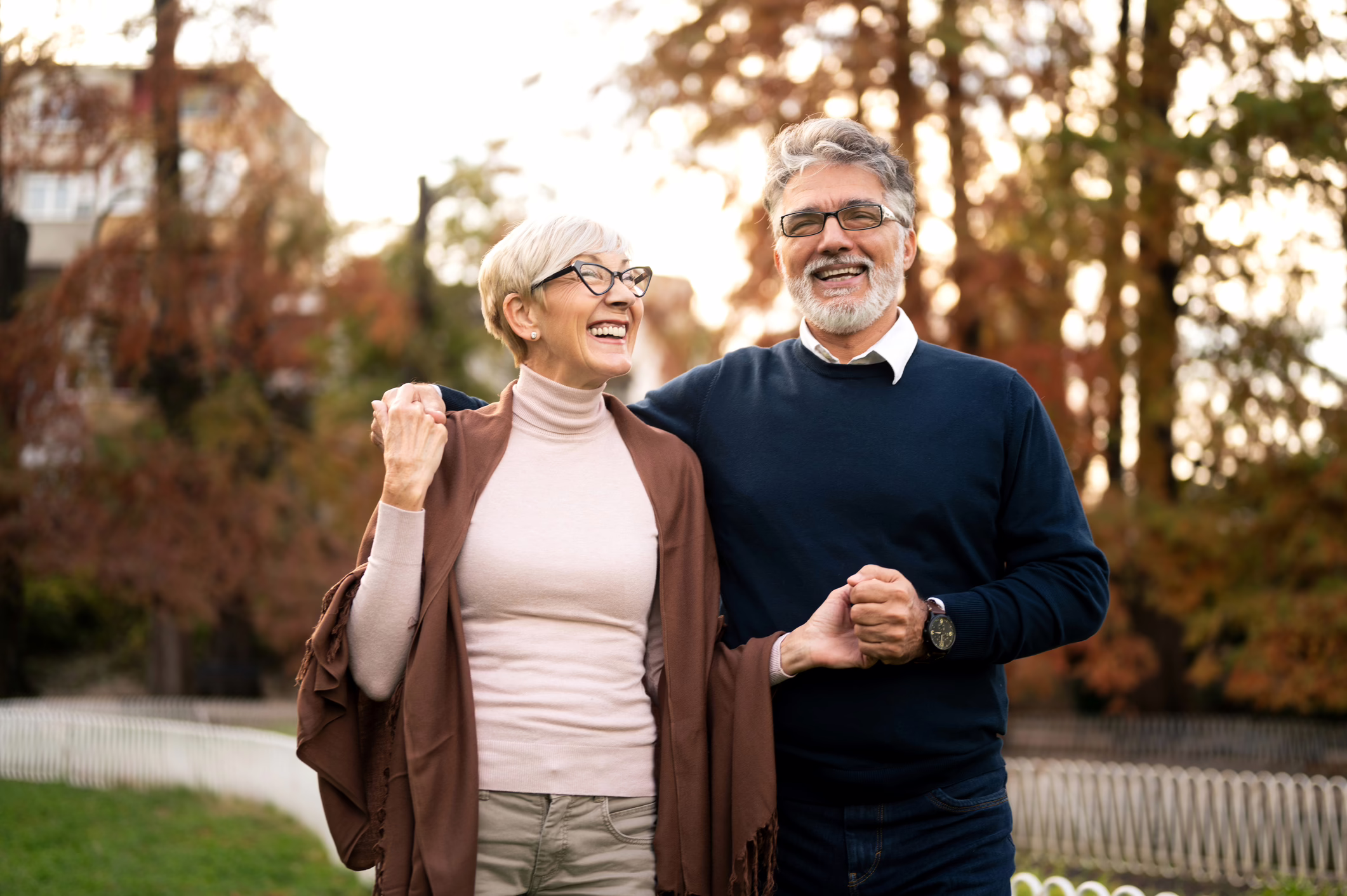 A gray-haired couple holding hands and walking outdoors together, smiling