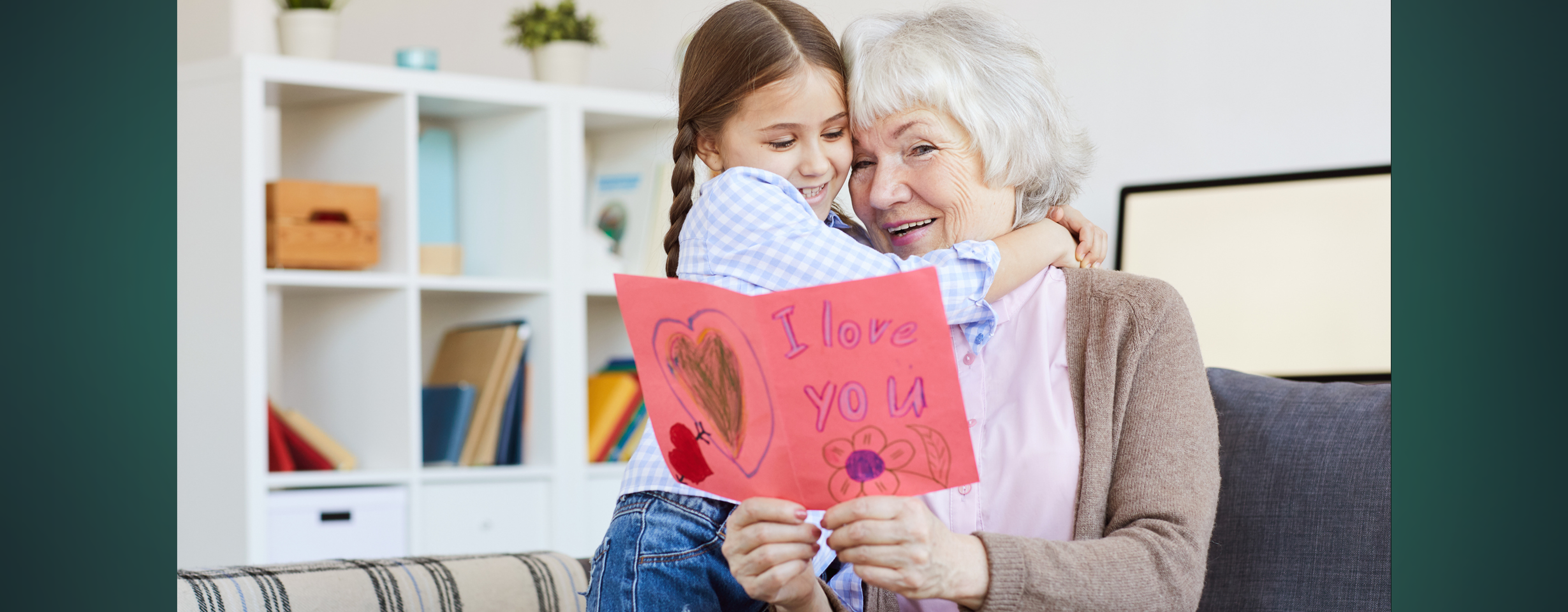 A grandma reading a Grandparents Day card from her granddaughter, who is giving her a hug.
