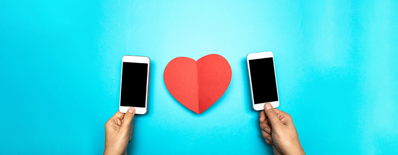A photo of two cell phones being held up with a paper heart in between them on a blue background
