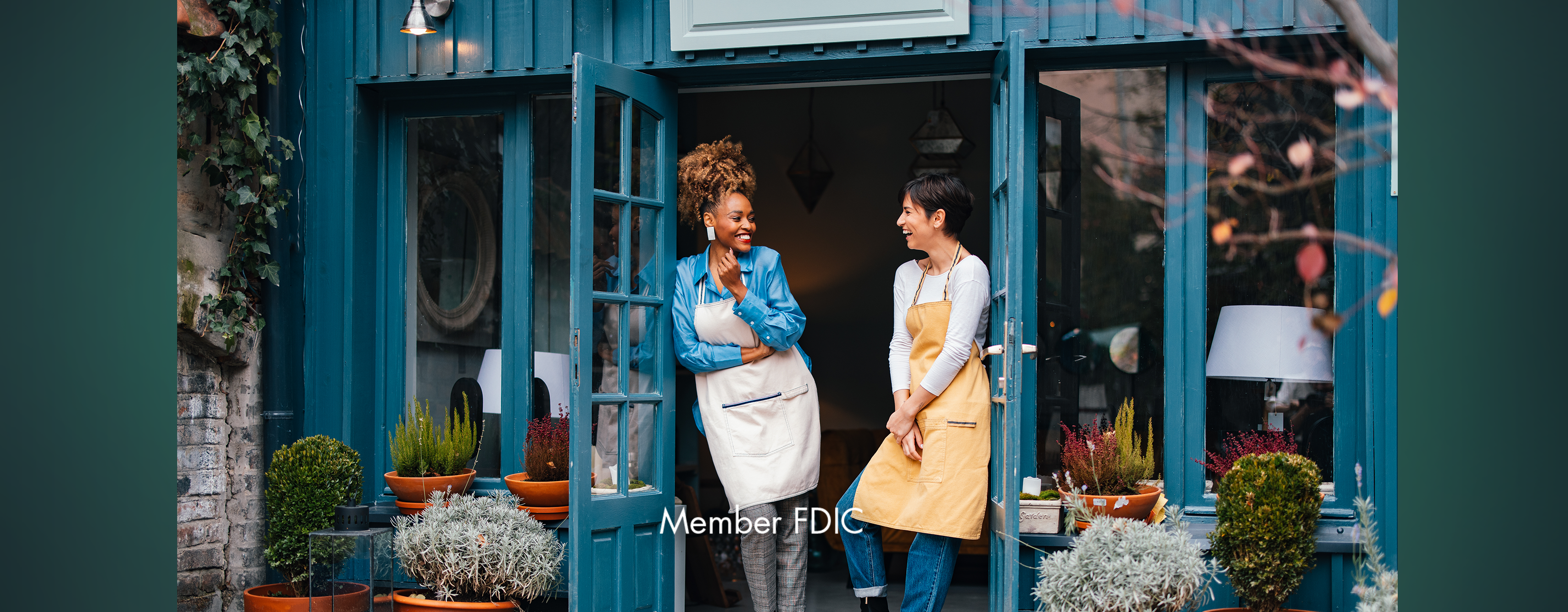 Two women in work aprons standing outside a plant shop talking